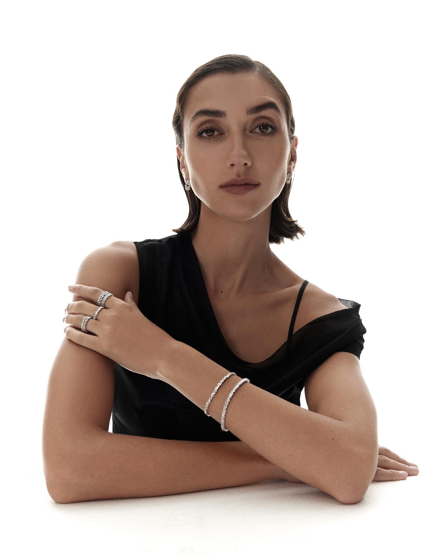 Woman wearing diamond rings and bracelets in a black top against a white background for Kennedy