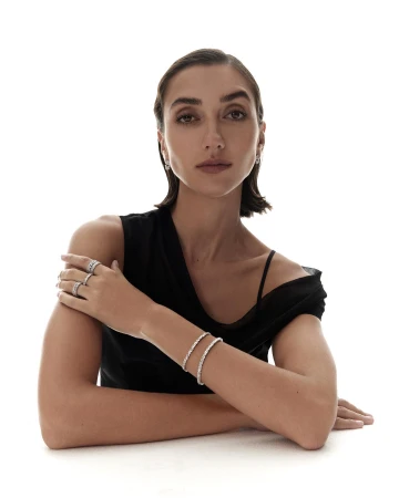 Woman wearing diamond rings and bracelets in a black top against a white background for Kennedy