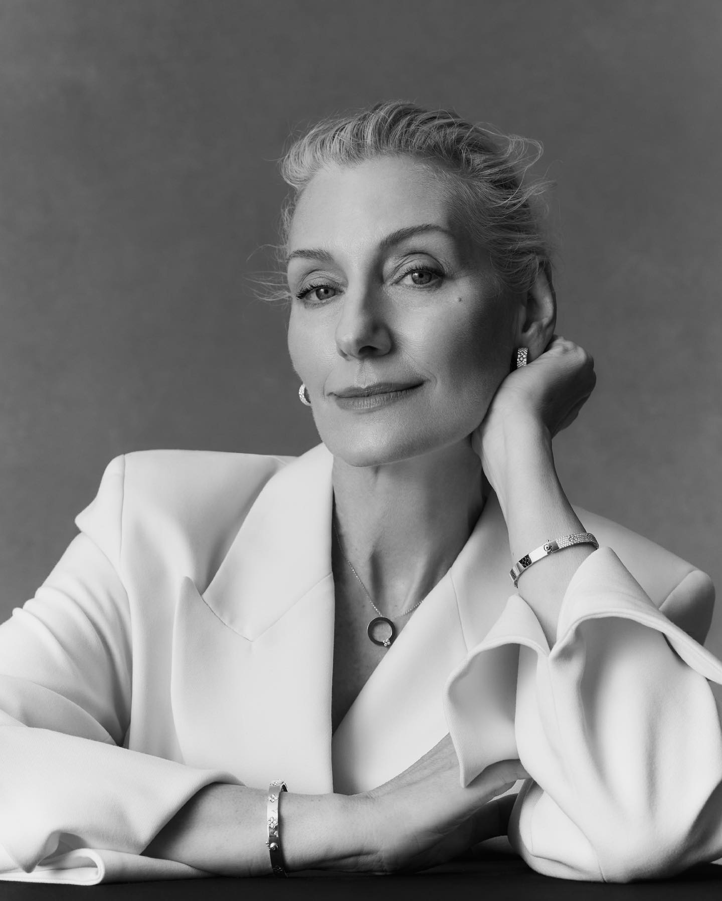 Black and white portrait of a mature woman with gray hair wearing a white blazer, jewelry, and posing in a photo studio.