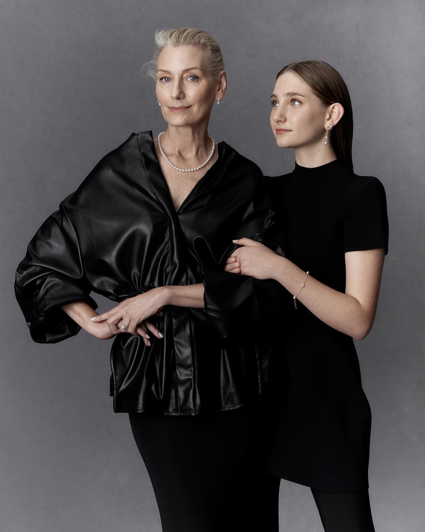 Elegant portrait of an elderly woman and a young woman in stylish black outfits against a neutral backdrop, showcasing fashion and grace.