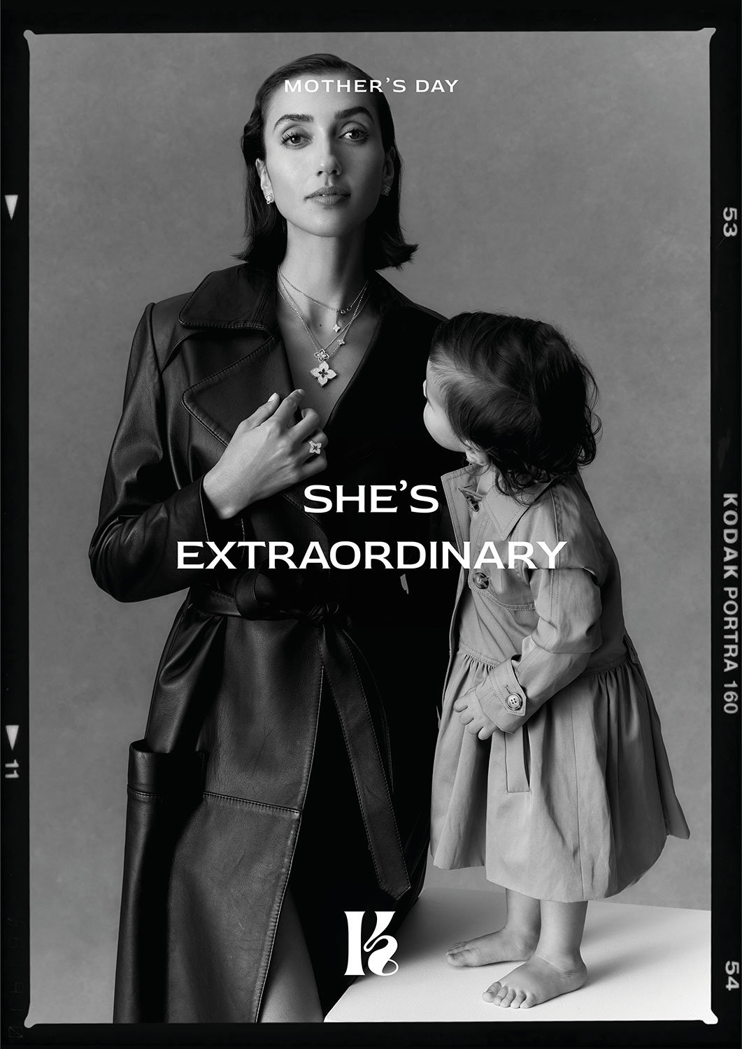 Black and white portrait of adult female in a trench coat, standing next to a child in a coat, posing in a photo studio.