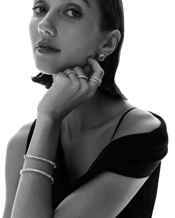 Close-up portrait of a woman wearing diamond rings, diamond bracelets, and earrings against a white background.