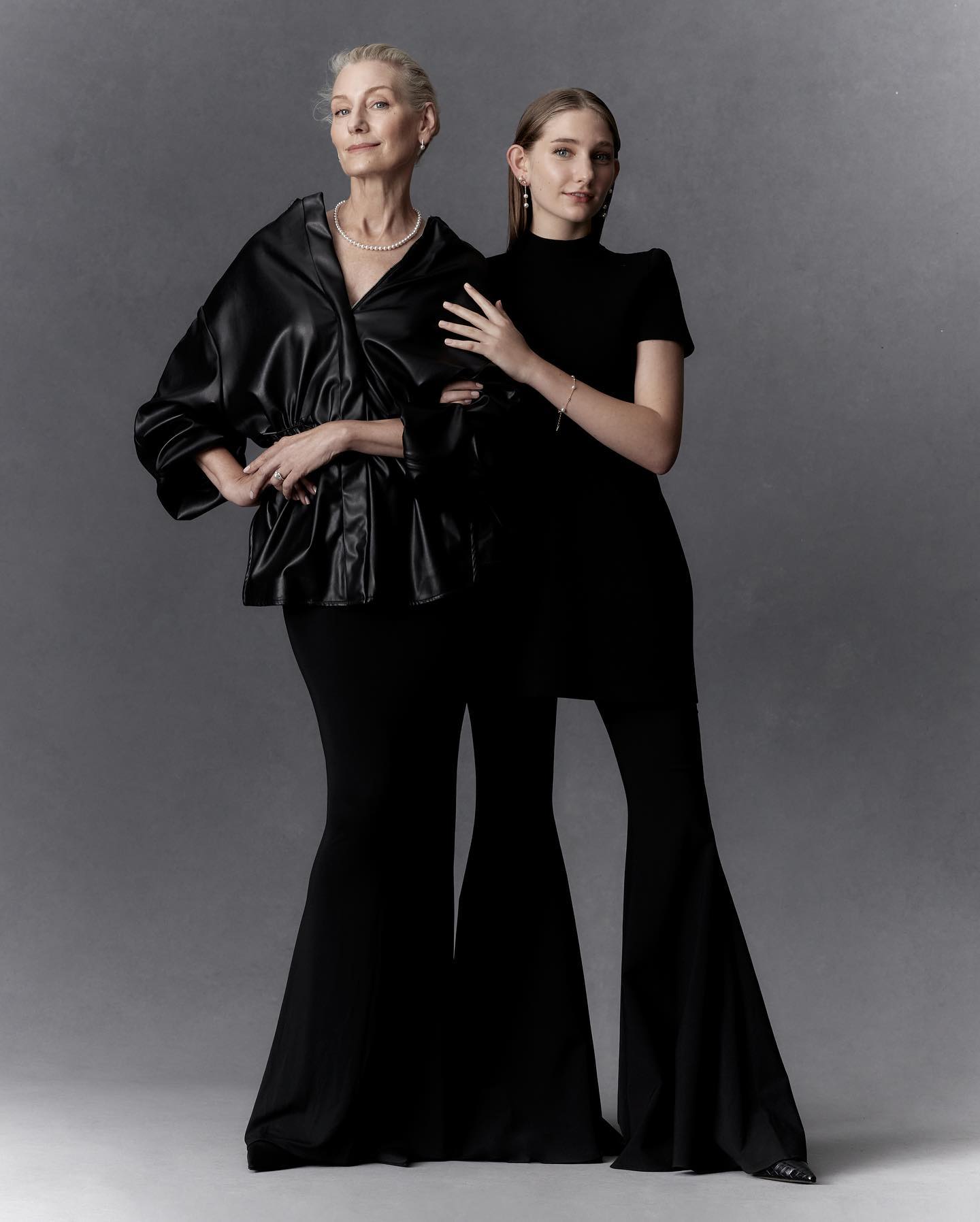 Elegant portrait of two women in all-black outfits posing in a studio, highlighting fashion and multigenerational beauty.
