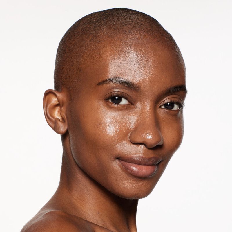 Close-up studio shot of a bald adult female with brown skin looking directly at the camera with a neutral facial expression.