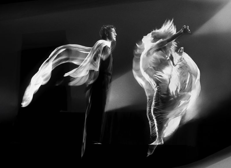 Black and white long exposure of a man and woman dancing, with motion blur showing their movement and flowing fabric.