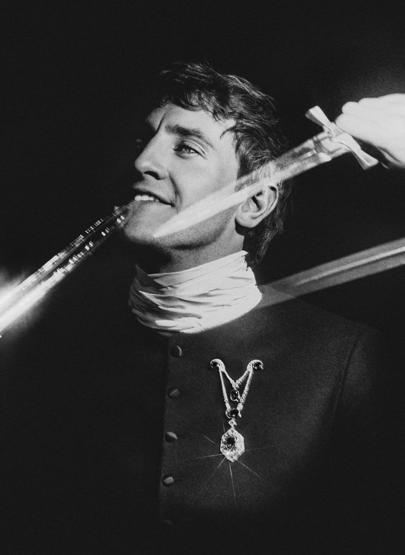Monochrome portrait of a smiling adult male with a white cravat and dark jacket, two swords crossing in front of his face.