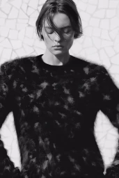 Monochrome portrait of Maya Vozhdaeva wearing a textured black patterned sweater in front of a white mosaic tile wall.