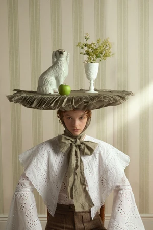 Lily Nova wearing a table headpiece topped with a ceramic dog and green apple in an editorial shot by Claire Harrison.
