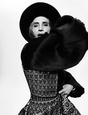 Black and white portrait of Ángela Molina in a wide-brim hat and embroidered corset top posing against a white studio background.