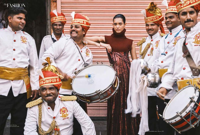 An Indian fashion shot features a female model posing with a marching band, all in costume, against a textured, muted background.