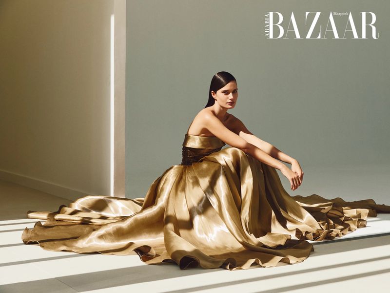 A striking fashion shot features a woman with slicked-back hair sitting on the floor in an opulent gold gown, highlighted by sunlight and studio lighting.