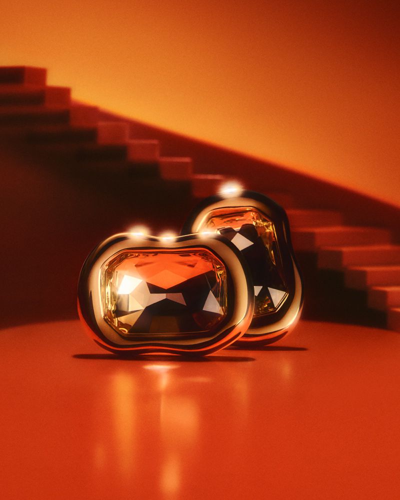 Two gold jewelry pieces with amber gemstones are displayed on an amber surface, illuminated by warm lighting and set against an amber background.
