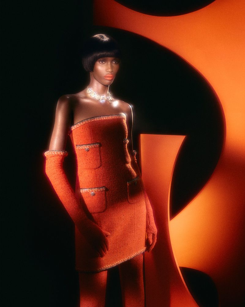 Fashion shot featuring an African American woman in an orange strapless dress with matching gloves, posed against an orange graphic backdrop.