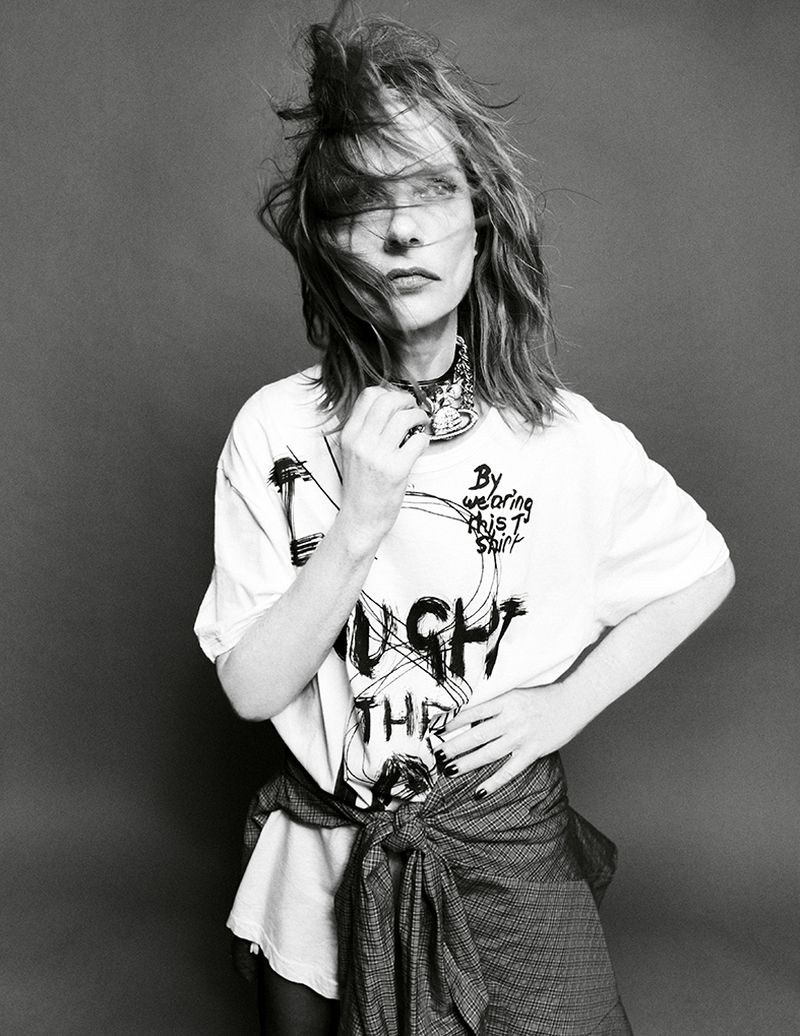 Monochrome portrait of a woman in a printed t-shirt and tied jacket, against a gray background, with medium shot camera framing.
