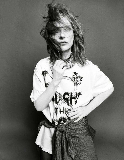 Monochrome portrait of a woman in a printed t-shirt and tied jacket, against a gray background, with medium shot camera framing.