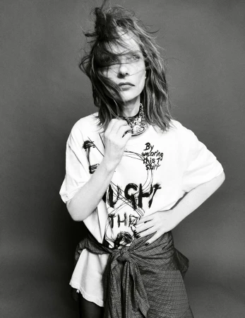 Monochrome portrait of a woman in a printed t-shirt and tied jacket, against a gray background, with medium shot camera framing.