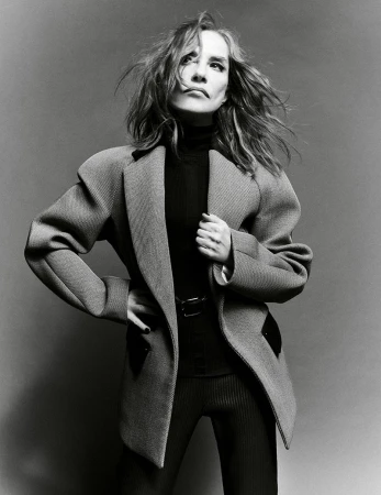 Monochrome studio shot of an adult female in a blazer, turtleneck, and leggings, striking a confident pose against a neutral backdrop.