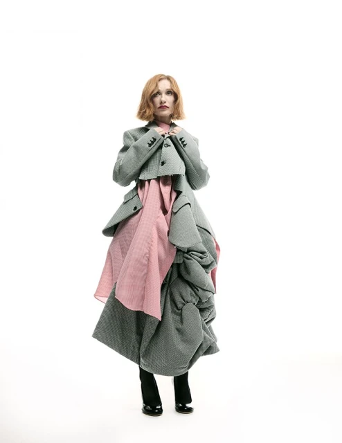 Fashion portrait of a woman in an oversized gray tweed blazer and skirt over a pink dress against a white background in a studio.