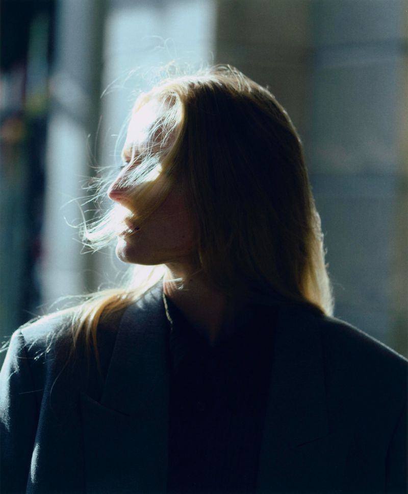 Woman with blonde hair in a blazer with backlit rim lighting, side profile in front of a blurred background.