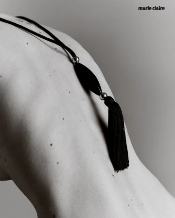 Monochrome shot of a person's back and shoulder adorned with a black tassel necklace and the Marie Claire logo in the upper corner.