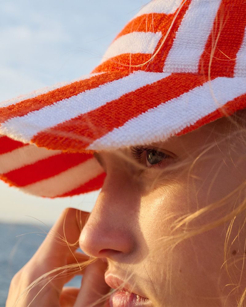 Close-up of a fair-skinned person wearing a striped orange and white sunhat in outdoor lighting, with a background of sky.