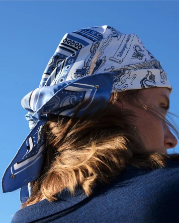 Woman wearing a blue and white patterned headscarf tied at the nape of her neck against a clear blue sky in an outdoor setting.