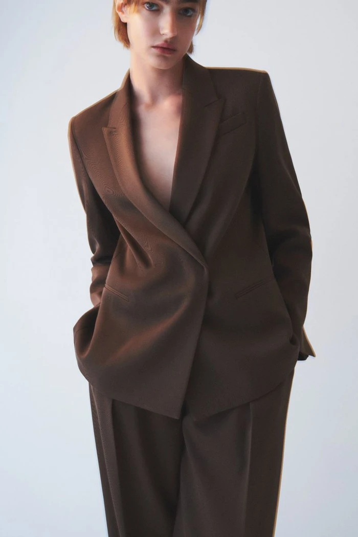 Model wearing a structured brown blazer and matching trousers against a plain white background