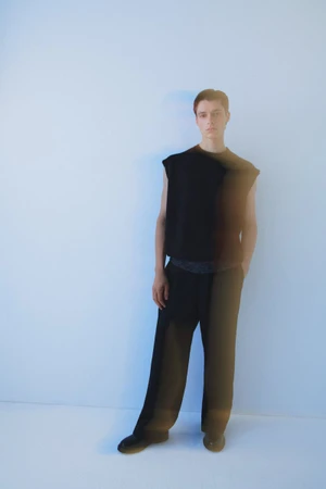 Model standing against a plain background in black clothing with a motion-blur duplicate effect.