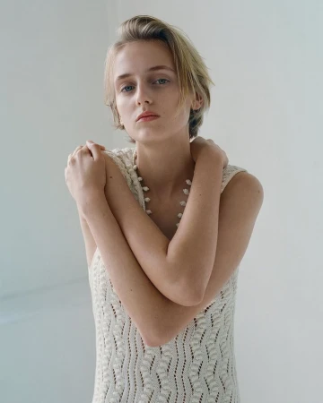 Model with short blonde hair wearing a cream sleeveless knit dress against a plain neutral background