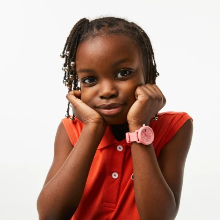 Portrait of a young Black girl in a red polo shirt, resting her chin on her hands and wearing a pink wristwatch against a white backdrop.