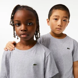 Two children wearing matching grey t-shirts with embroidered crocodile logos against a clean white seamless studio background.