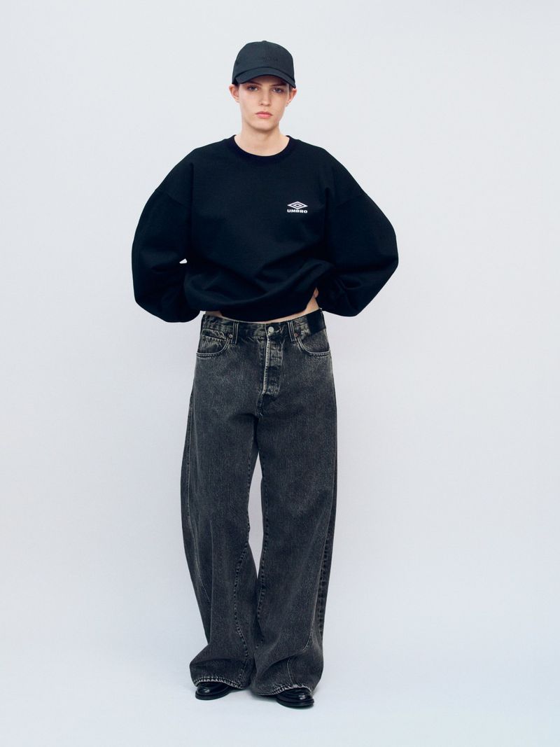Model wearing a black sweatshirt, black baseball cap, and baggy washed black jeans against a white seamless background.