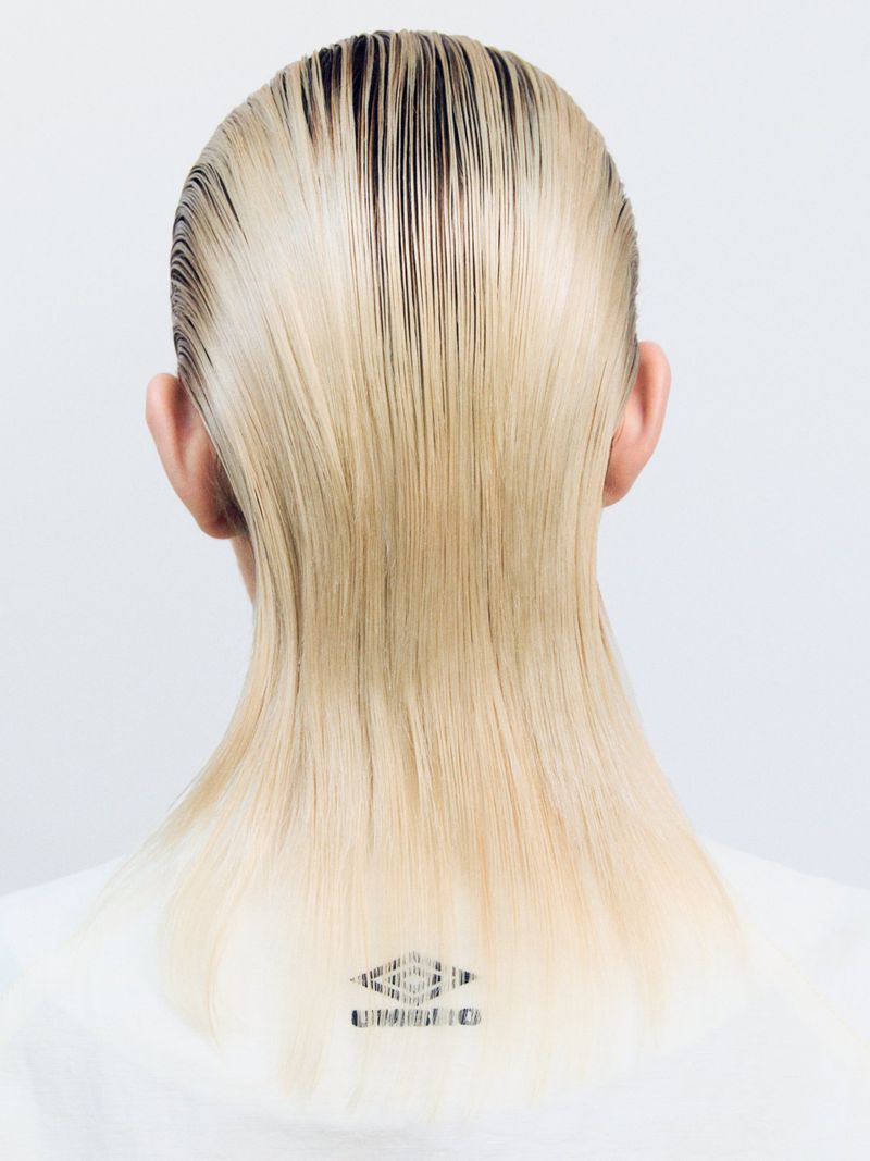 Back view of a person with light blonde hair slicked back against a clean white background, featuring a visible Umbro logo.