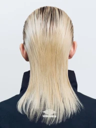 Rear view of slicked-back blonde hair styled straight down over a high-neck black jacket with an Umbro logo on a studio backdrop.