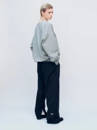 Model wearing an oversized light grey sweatshirt and loose black track pants viewed from behind against a neutral studio backdrop.