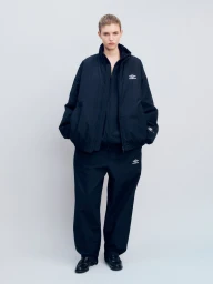 Model wearing an oversized dark navy track jacket and matching nylon trousers against a neutral studio backdrop.