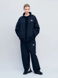 Model wearing an oversized black ssstein x Umbro nylon tracksuit against a pale grey seamless studio backdrop.