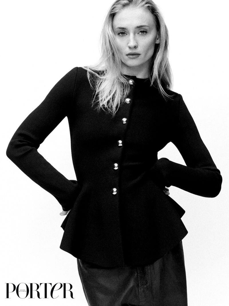 Portrait of a young woman in a black peplum jacket with metal buttons against a bright white background. Fashion editorial style.