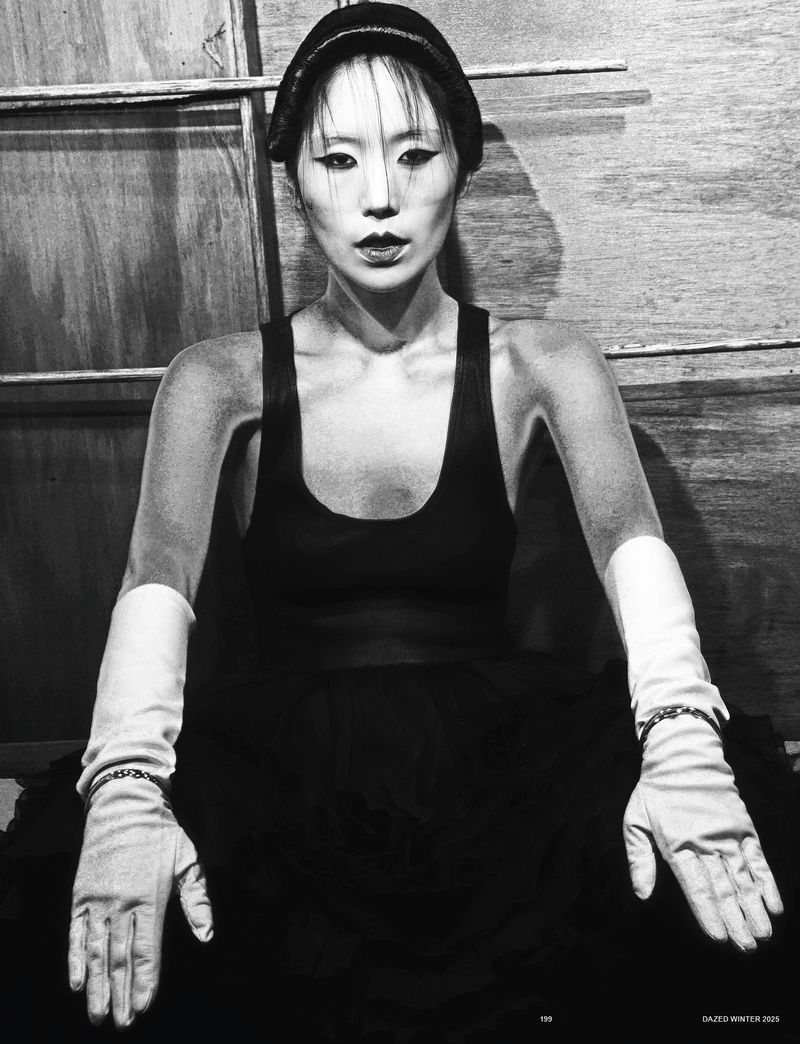 Striking portrait of an Asian woman with unique makeup and a knit cap in a black top, set against a textured wooden background.