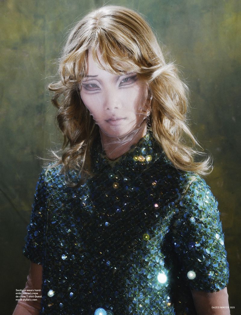 Close-up studio shot of a blonde adult female model in a green beaded dress with a neutral facial expression and painted makeup.