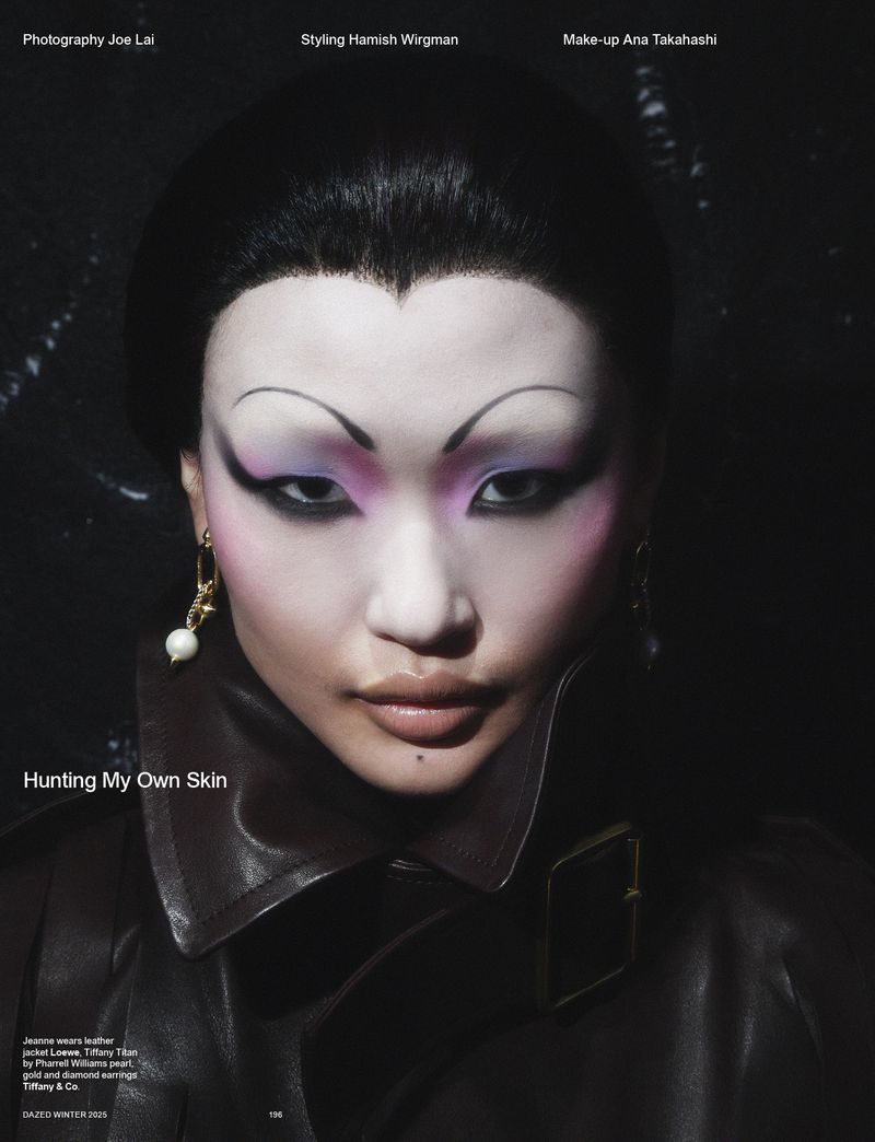 Close-up fashion portrait of an Asian woman with high-fashion makeup and a leather coat in a studio with dark lighting.