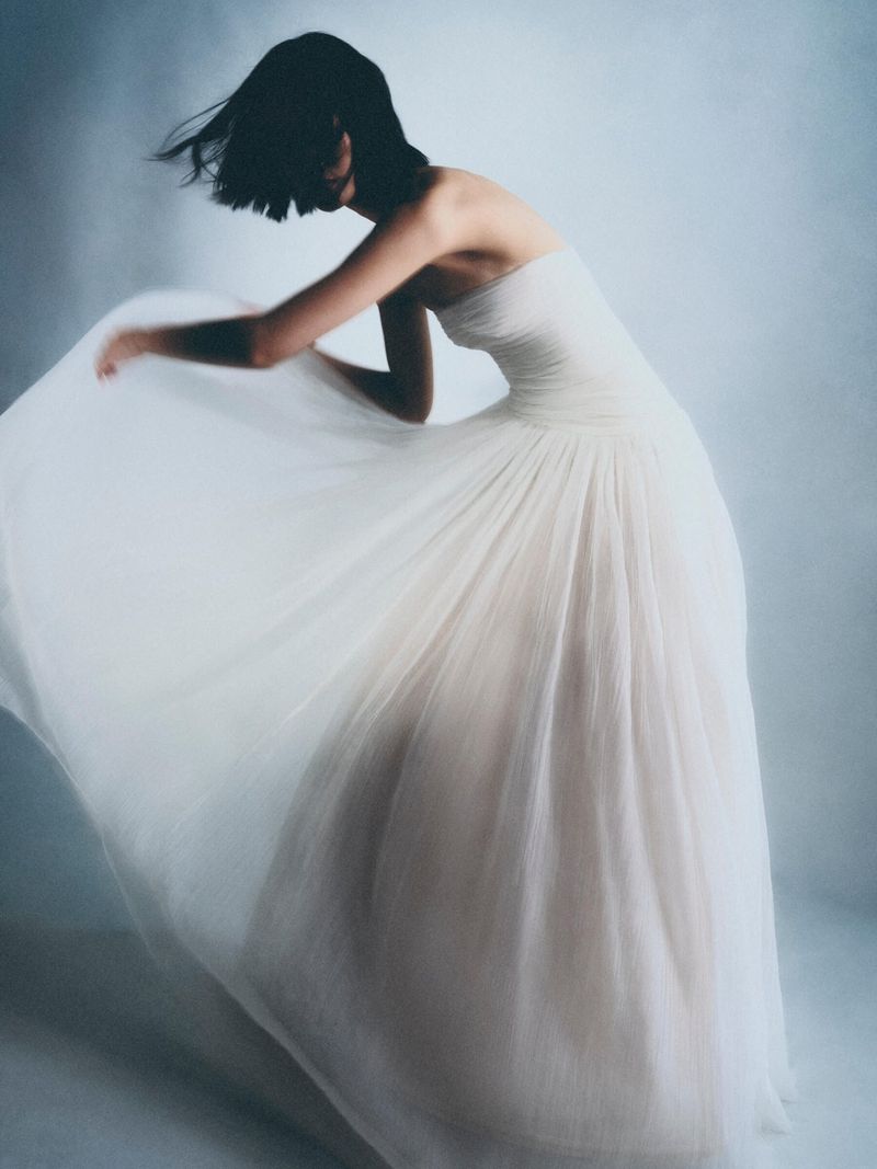 Fashion shot: woman in white strapless tulle gown posing in studio with dreamy lighting and minimalist background. Fashion, beauty, and style.