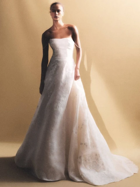 Elegant woman wearing a strapless, floor-length, off-white gown in a fashion forward pose against a neutral-toned studio backdrop.