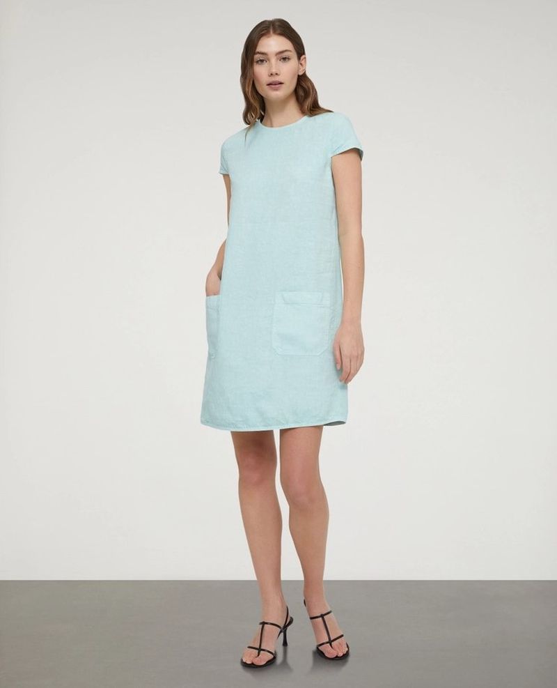 Full-length studio shot of an adult woman posing in a short-sleeved light-blue dress and black high-heeled sandals against a neutral background.