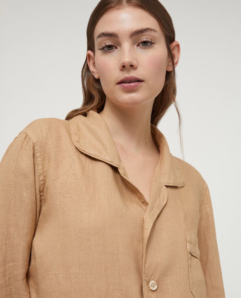 Close-up portrait of a young adult woman with fair skin, wearing a beige button-down shirt, posing in an indoor setting.