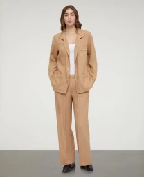 Model wearing a tan linen suit jacket and matching trousers over a white top against a neutral studio backdrop