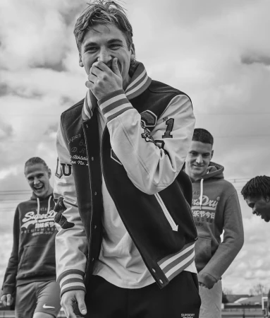 Black and white shot of a young man laughing with his hand over his mouth, standing outdoors with three other men.