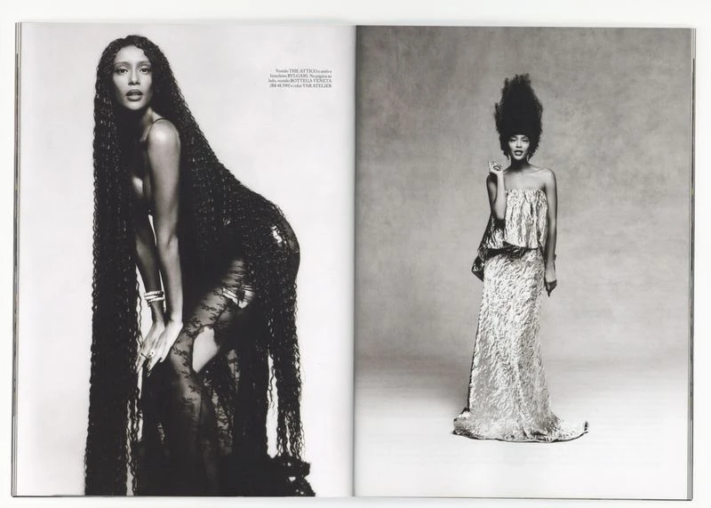 Black and white full shot of two women, one with waist-long hair and lace dress, the other in a full-length gown with large hair.