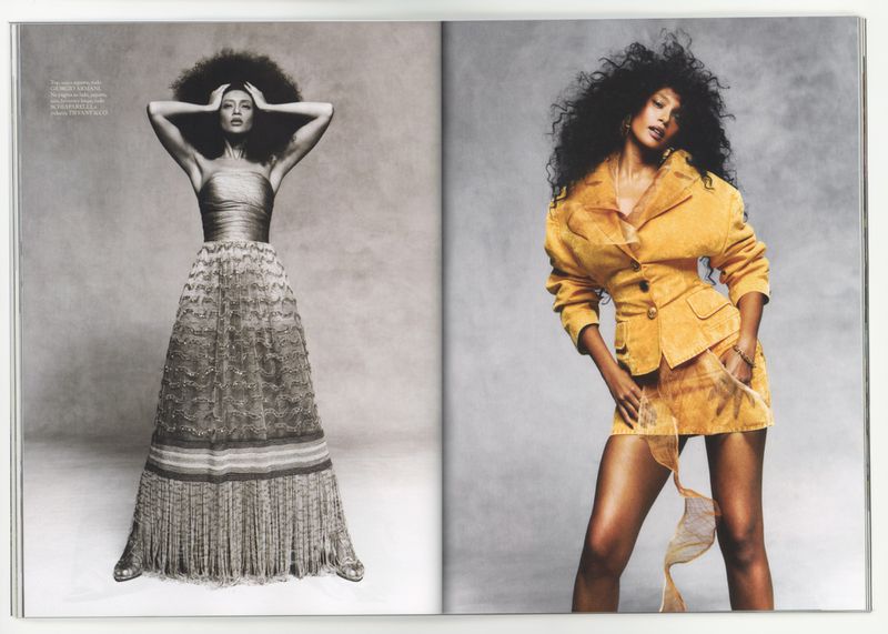Editorial fashion spread with two women in gowns, one in a tan gown, the other in a golden suit, against a grey backdrop.