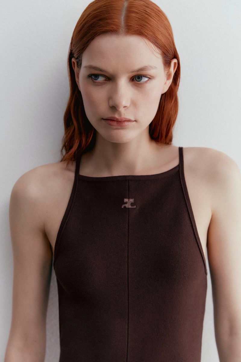 A fair-skinned woman with auburn hair poses in a studio wearing a brown halter dress against a neutral background in a close-up shot.